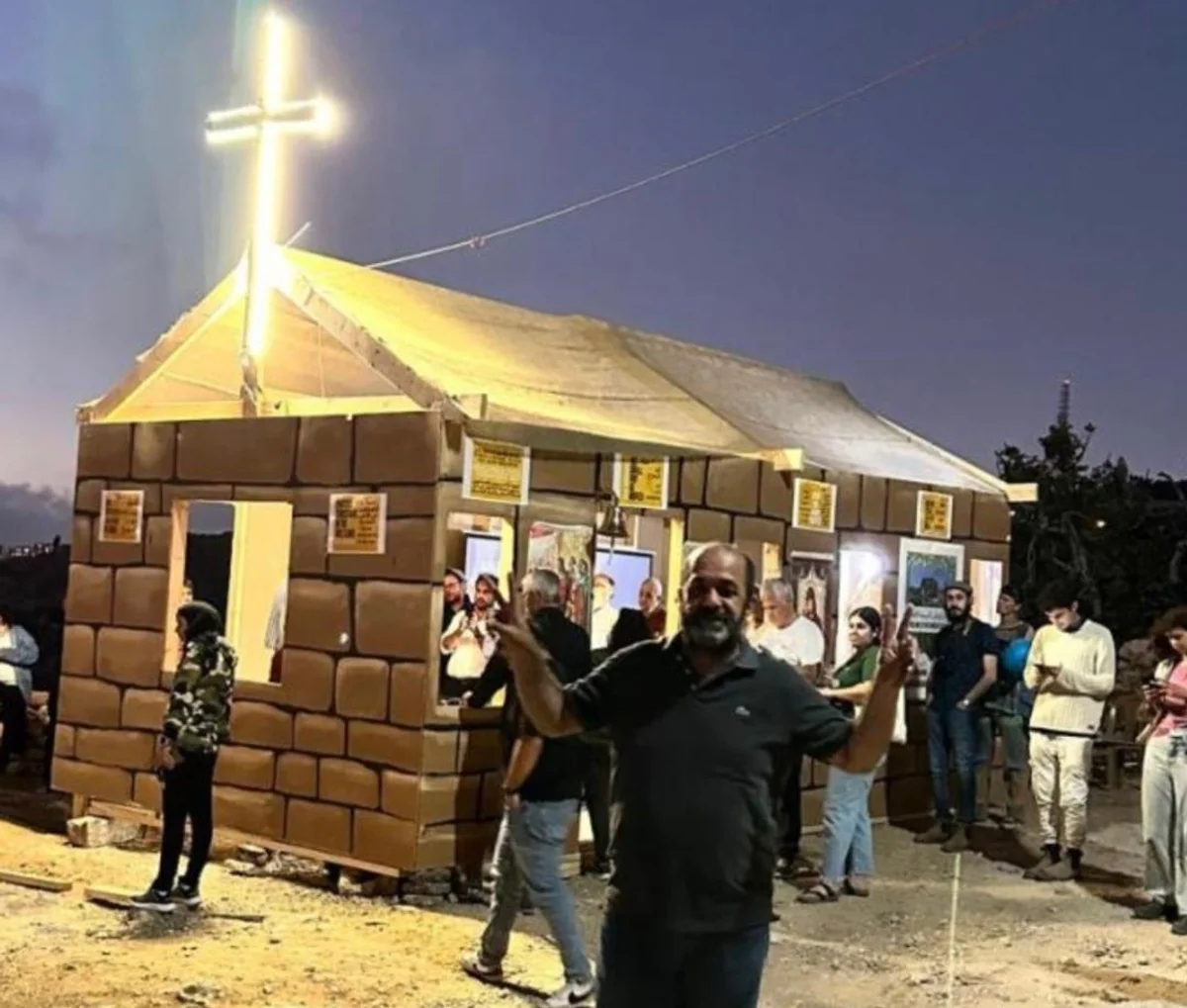 Supporters gathered at night around a symbolic church with an illuminated cross on the Kisiya family's land